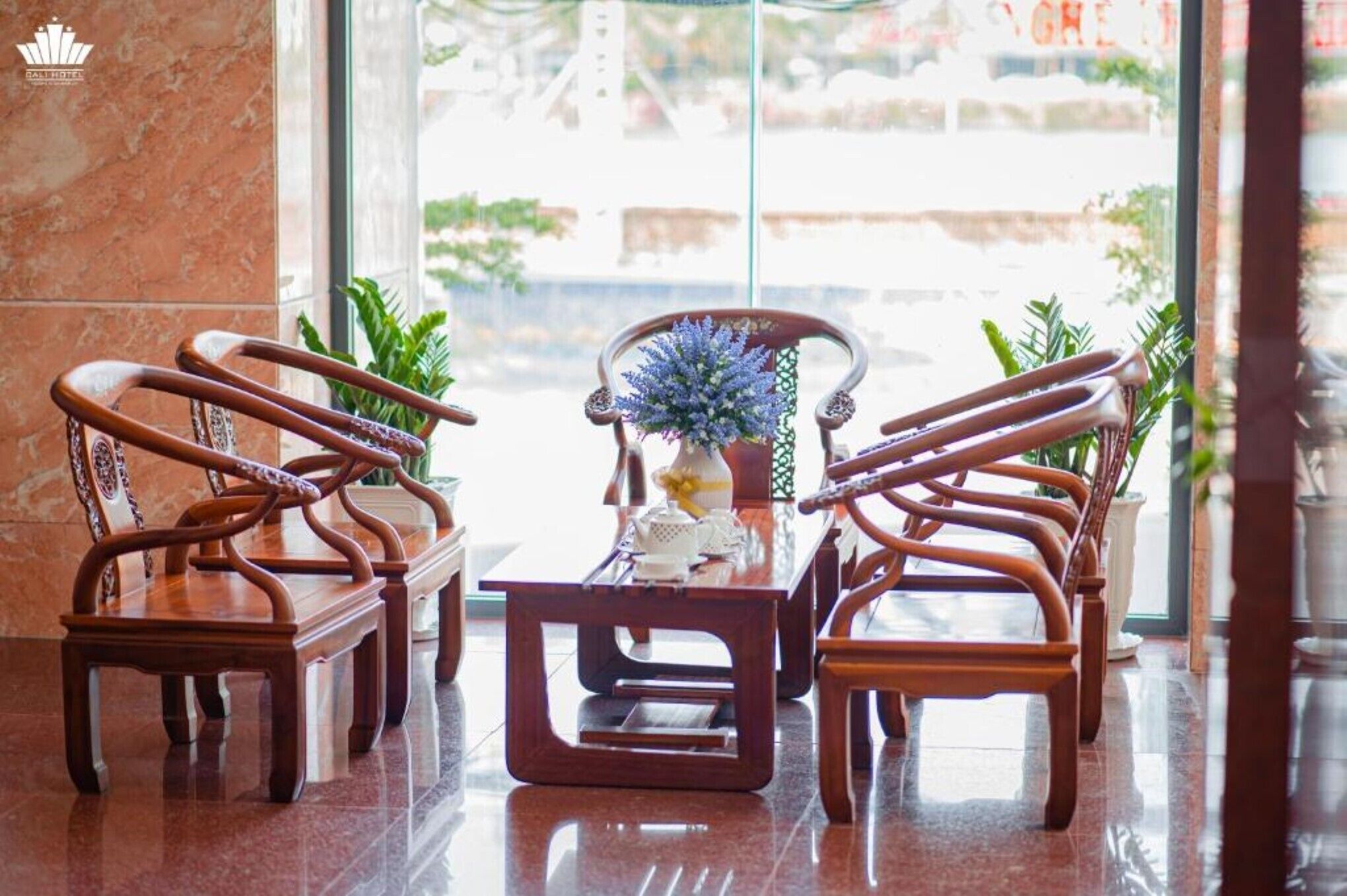 Un hall con cuatro sillas de madera y una mesa central, un jarrón con flores y vistas a un puente por la ventana.