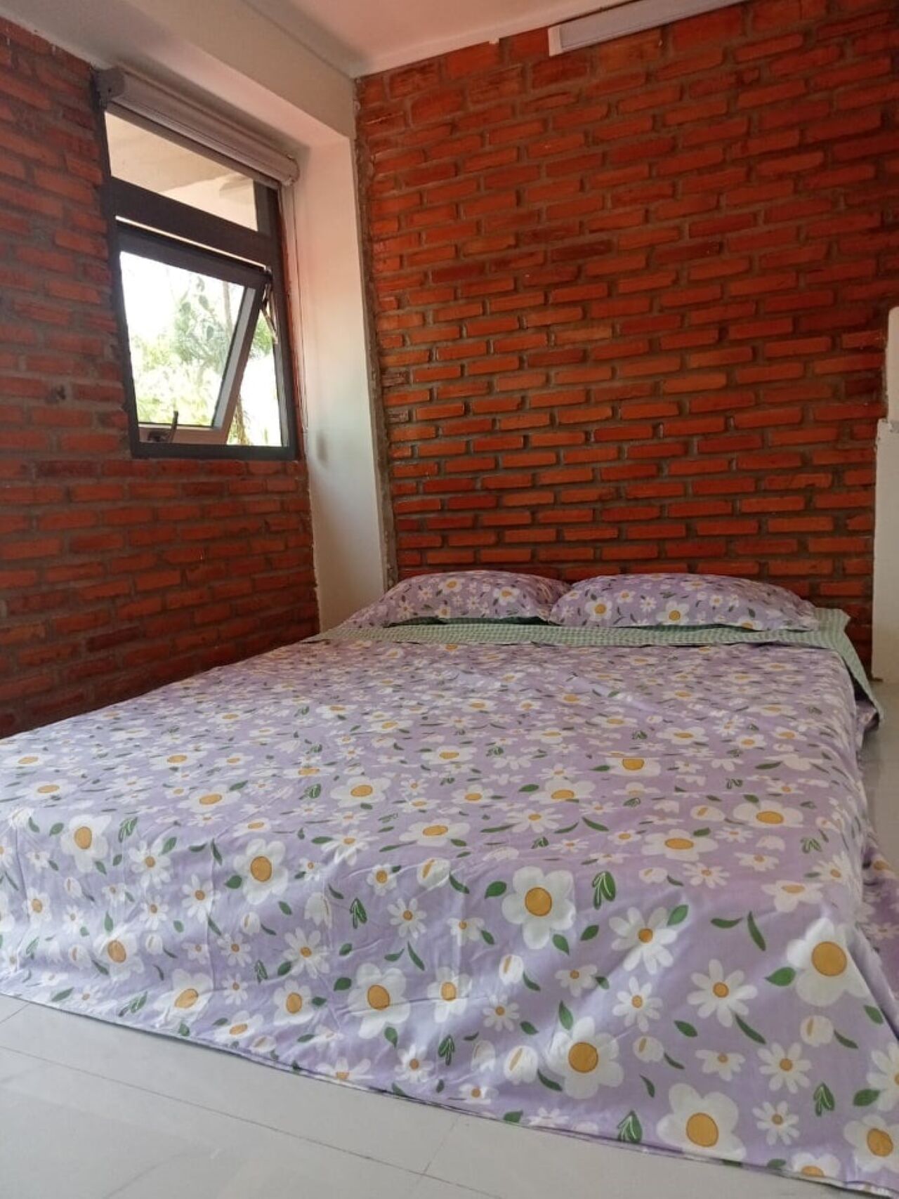 A bedroom with a brick wall, a window, and a floral bedspread.
