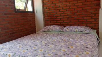 A bedroom with a brick wall, a window, and a floral bedspread.