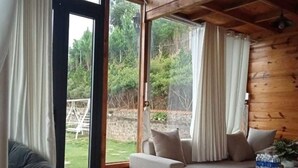 A cozy cabin interior with a wooden ceiling, a sofa, a chair, and a glass table.