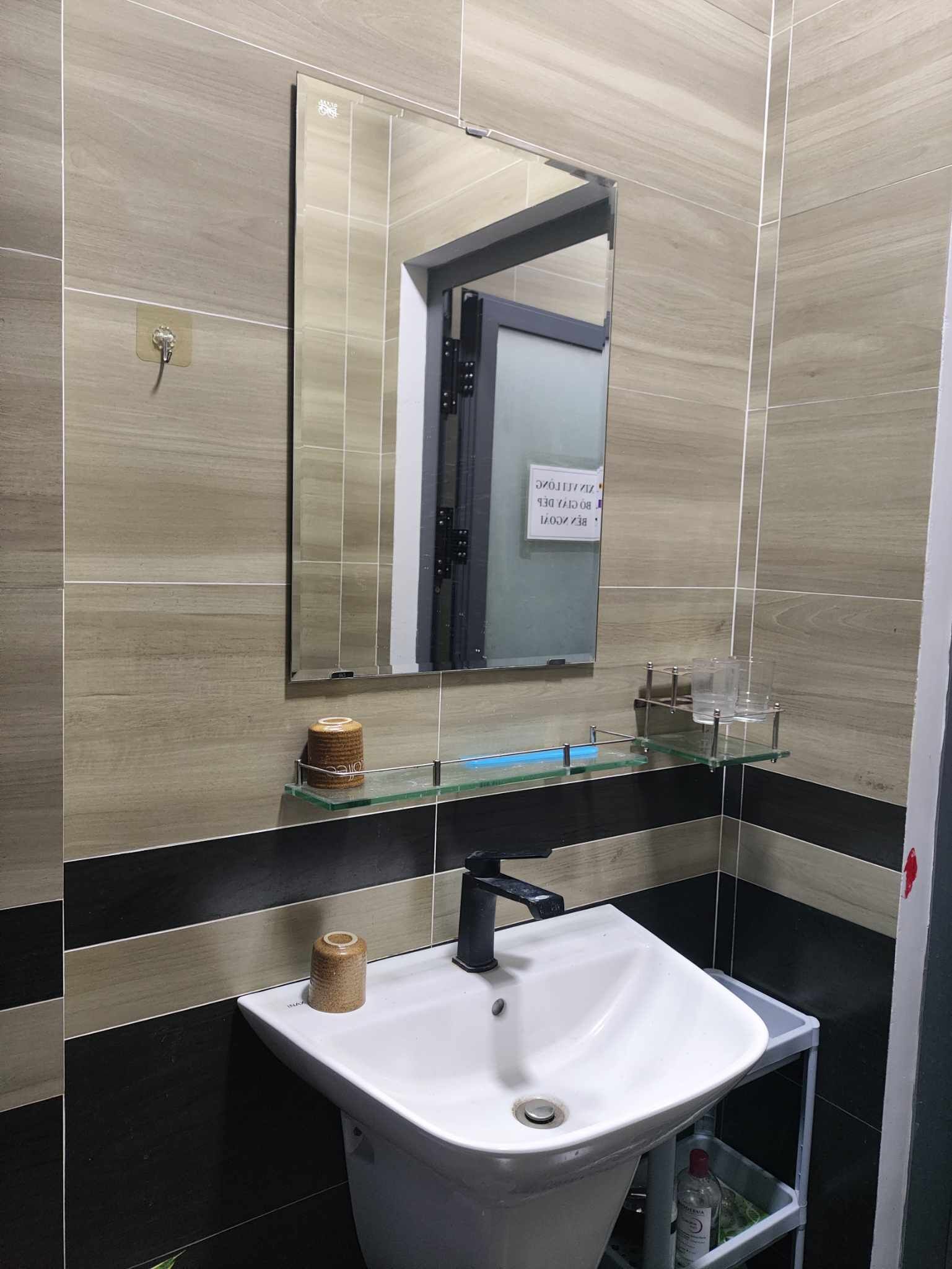 A bathroom with a white sink, a mirror, and a glass shelf with toiletries.