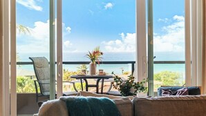 A room with a large sliding glass door leading to a balcony with a view of the ocean.