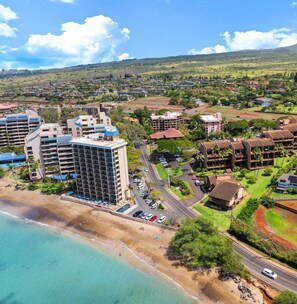 An aerial view of a coastal resort area with beachfront properties, a large hotel, and a golf course.