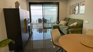 A modern living room with a glass door leading to a balcony, a green sofa, a wooden dining table, and a black cabinet. - Benidorm Beach Belluba Luxury bay (Benidorm)