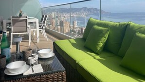 A balcony with a green sofa, dining table, and chairs, overlooking a cityscape and the sea. - Benidorm Beach Belluba Luxury bay (Benidorm)
