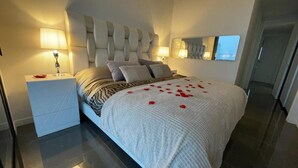 A modern bedroom with a large bed, a nightstand, a wall-mounted mirror, and a door leading to another room. - Benidorm Beach Belluba Luxury bay (Benidorm)