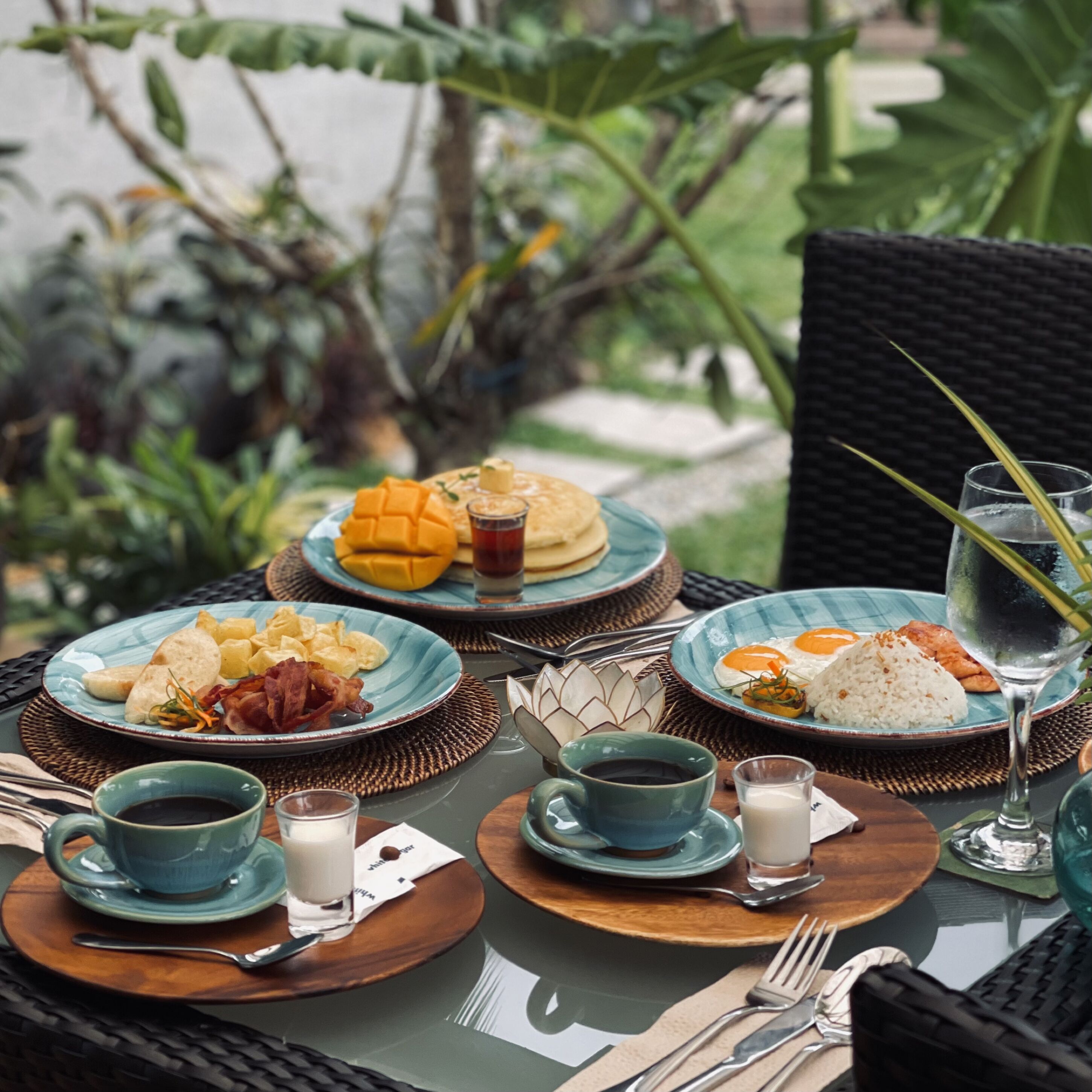 Une table dressée avec des assiettes, des tasses et des couverts pour le petit-déjeuner.