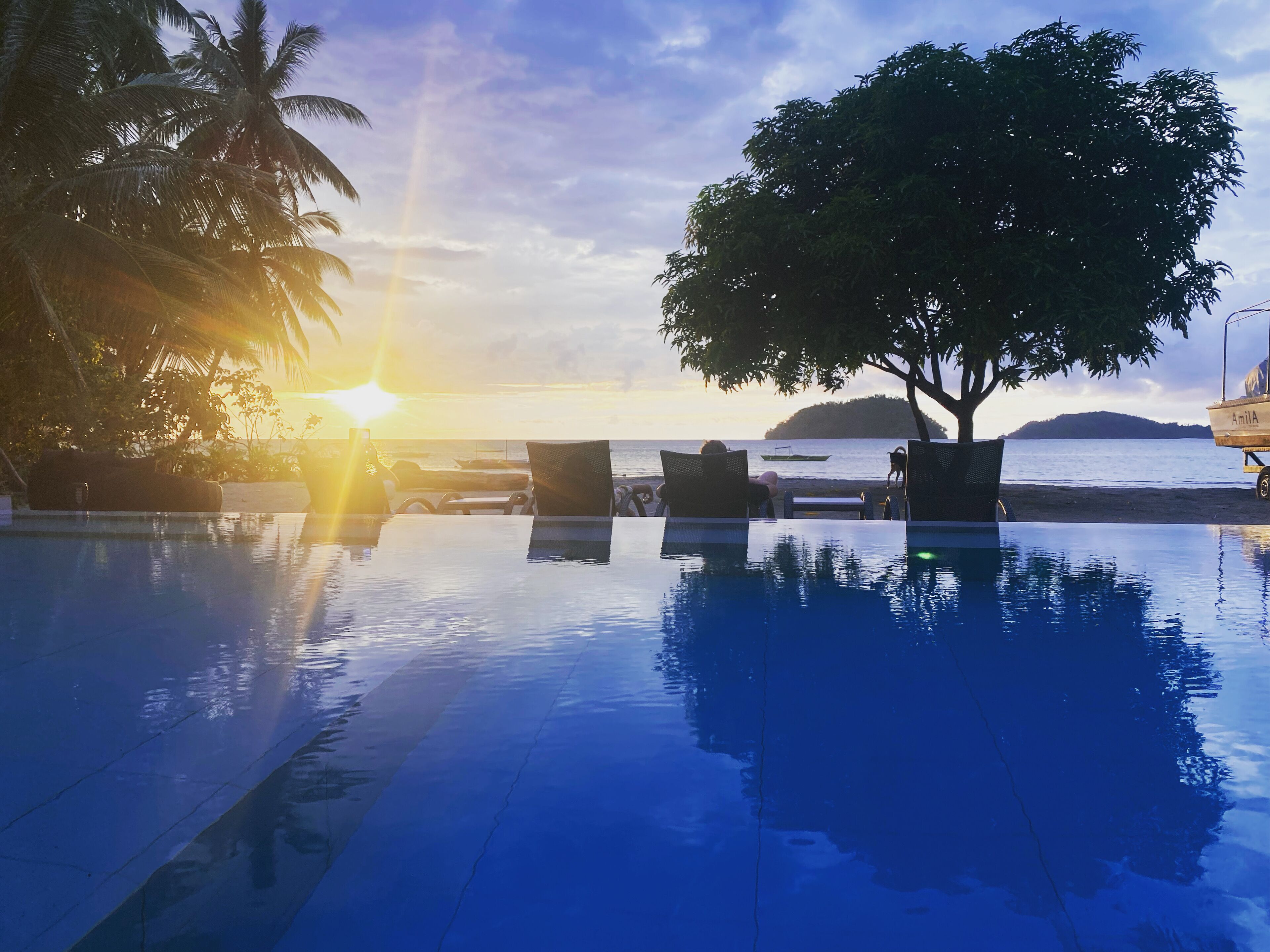 Zona de piscina con sillas reclinables y vista al atardecer sobre el mar.