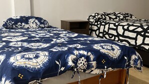 Une chambre avec un grand lit recouvert d’une couvre-lit à motifs floraux, un lit plus petit avec une couvre-lit à motifs géométriques et une table de chevet en bois.