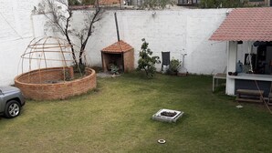 Un jardin à l’arrière de la maison, avec une construction en briques, un petit espace aménagé en jardin et une voiture garée à proximité.