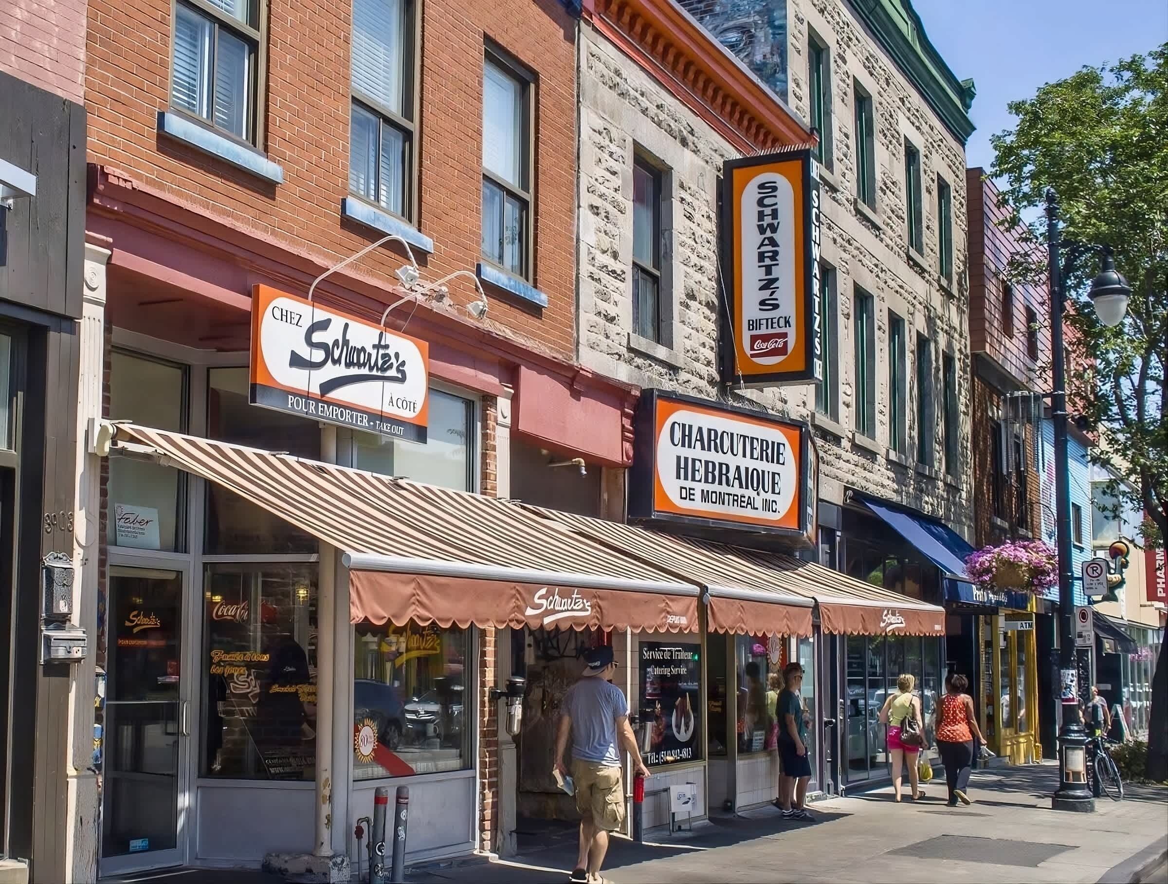 A street with storefronts, including a restaurant named 'Schwartz's' and a sign for 'Charcuterie Hebraique.'