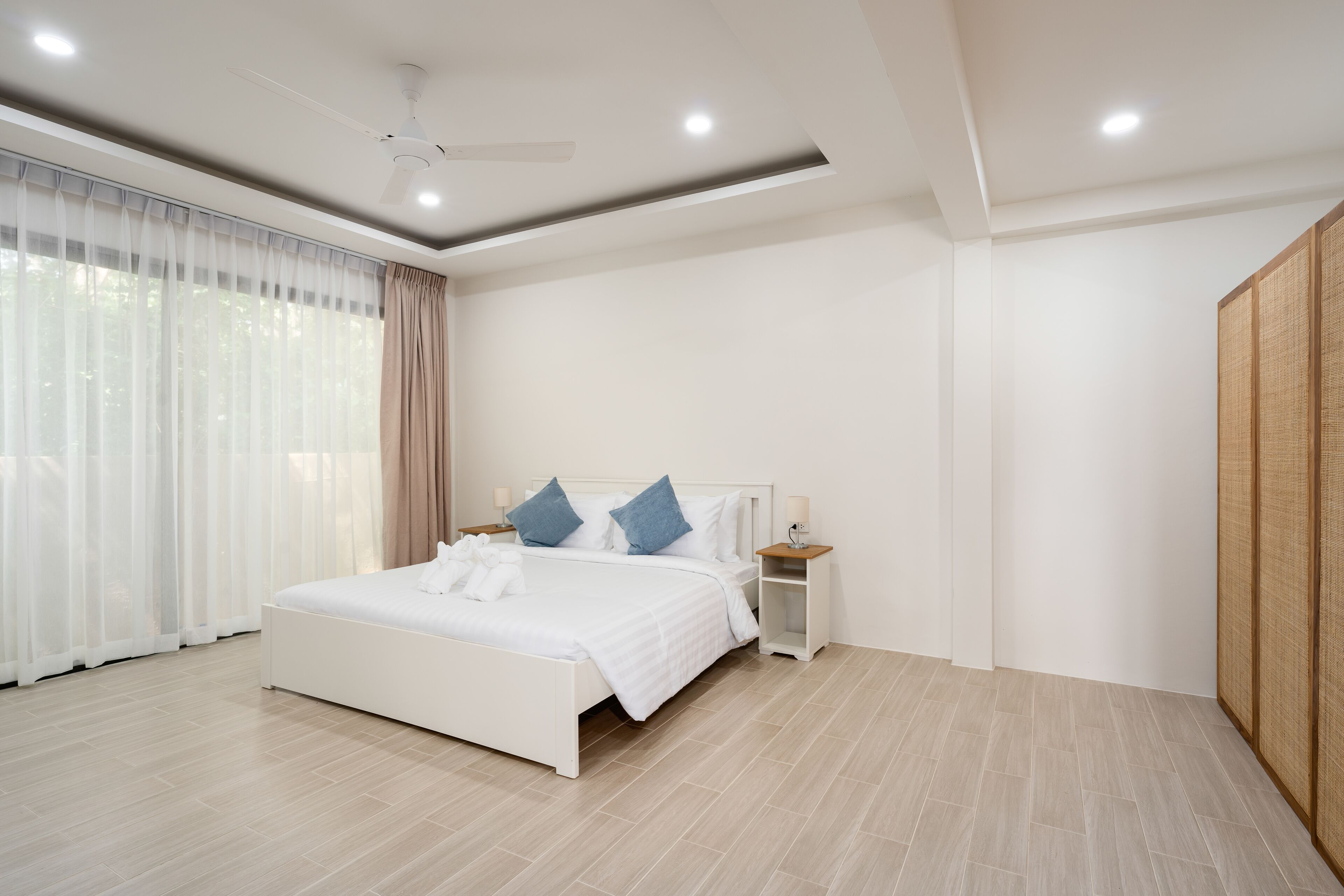 A modern bedroom with a large bed, bedside tables, a ceiling fan, and a wardrobe.