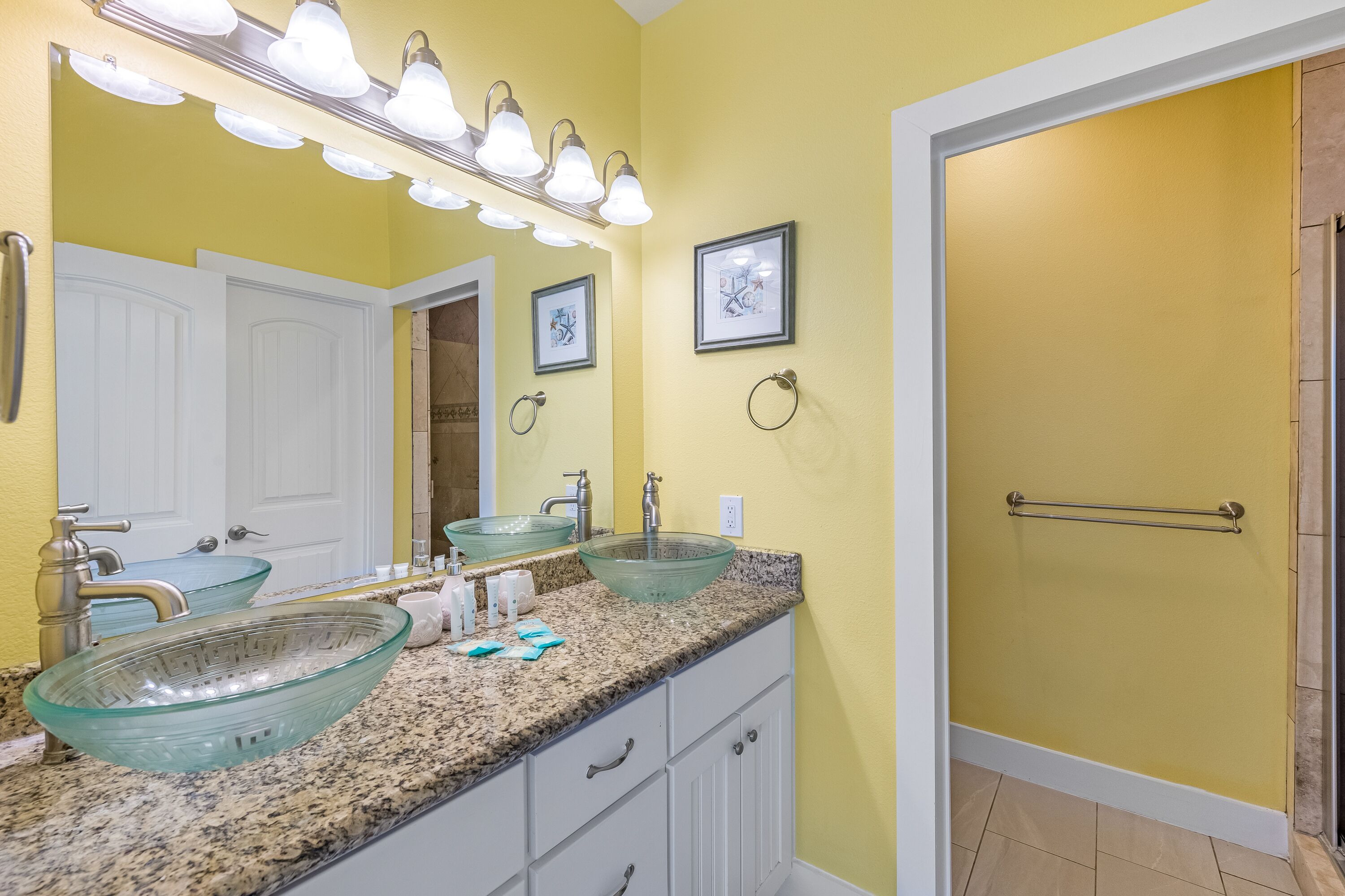 A bathroom with two glass sinks, a vanity with drawers, a mirror with lights, and a towel rack.