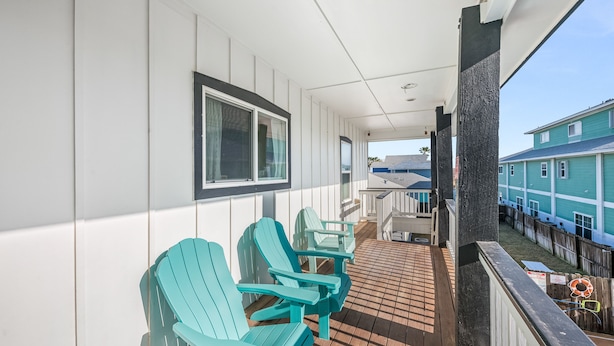 Varanda coberta com piso de madeira, paredes brancas e cadeiras Adirondack azul-turquesa.