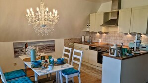 A kitchen with a dining area, featuring a chandelier, white cabinets, and a small island with appliances.