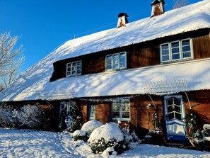 A two-story wooden house with a snow-covered roof and a blue door.