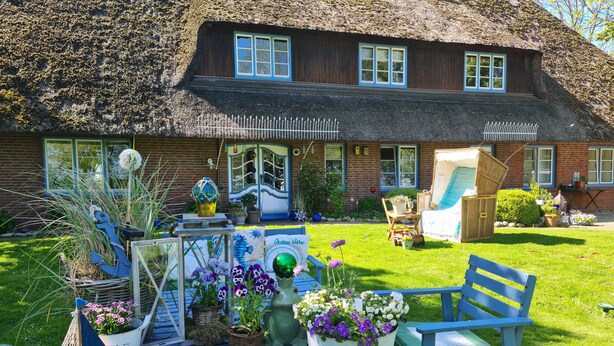 A thatched-roof house with a garden table set up with potted plants and a small sailboat model.