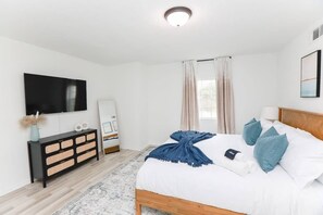 A bedroom with a bed, a TV, a dresser, and a window with curtains.