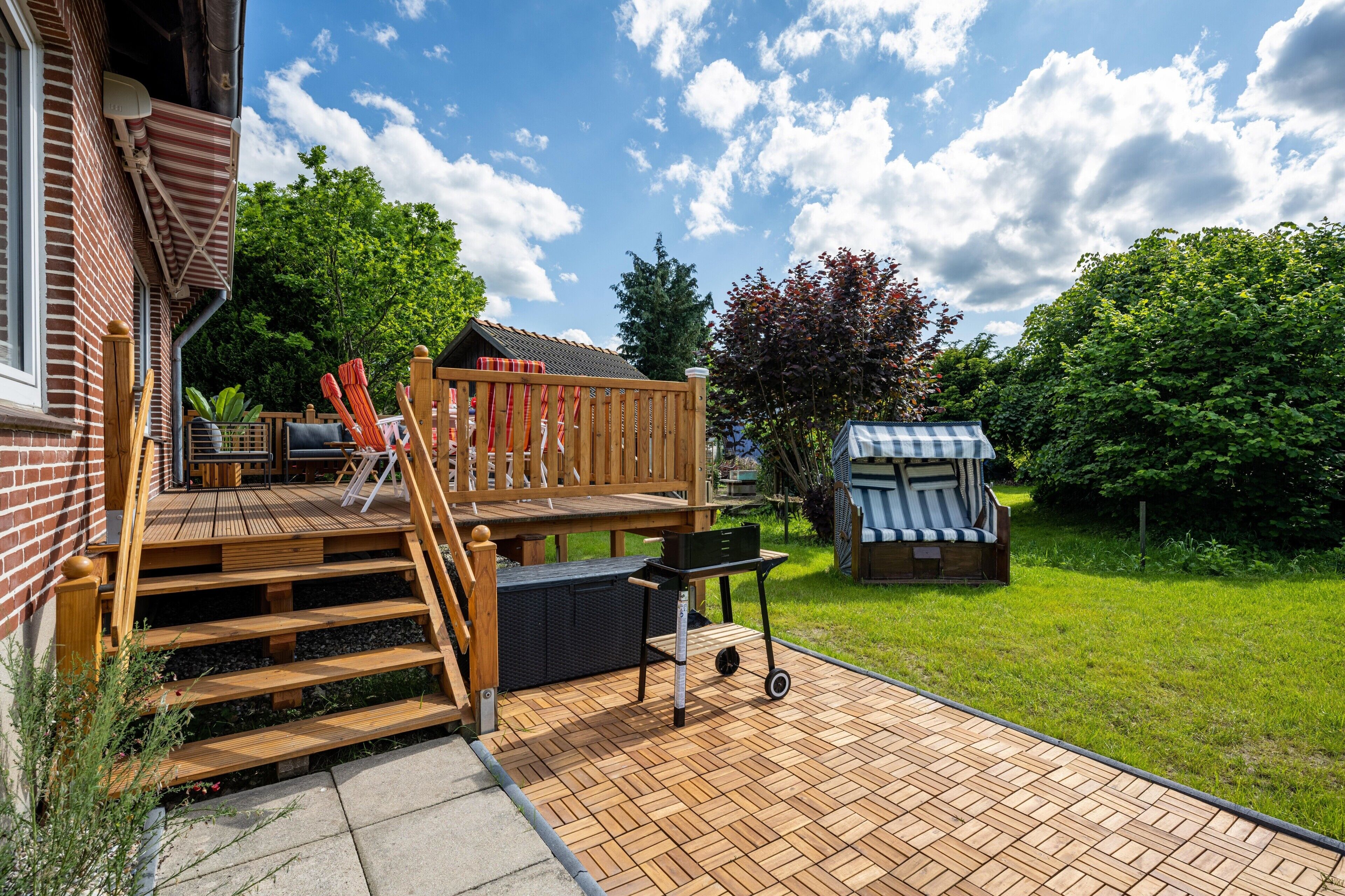 A wooden deck with a grill, a covered seating area, and a small shed.