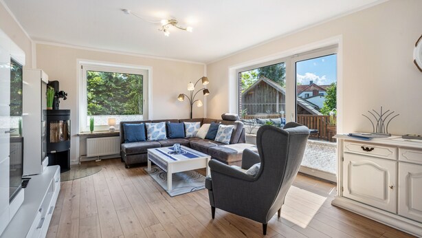 Un salon moderne avec un canapé d’angle, un fauteuil gris, une table basse blanche et un meuble blanc.