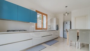 Una cocina moderna con armarios azules, horno empotrado y comedor con mesa y sillas.