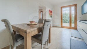 Un área de comedor con una mesa de madera y cuatro sillas, un tazón sobre la mesa, y vista al exterior a través de un vidrio.