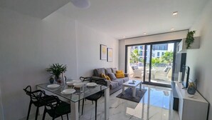 Un salon moderne avec une table à manger en verre, un canapé avec des coussins et un téléviseur posé sur un meuble.
