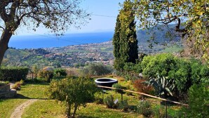 Un giardino con un vialetto in pietra, un elemento d'acqua circolare e vista su una cittadina costiera.