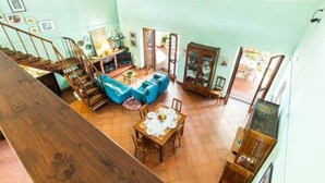 Un ampio soggiorno con divano blu, un tavolo da pranzo con sedie e una scala che conduce a un piano superiore.
