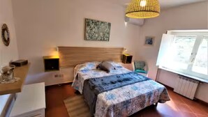 Camera da letto con un letto, comodini, una lampada a sospensione, una finestra e un'opera d'arte appesa al muro.