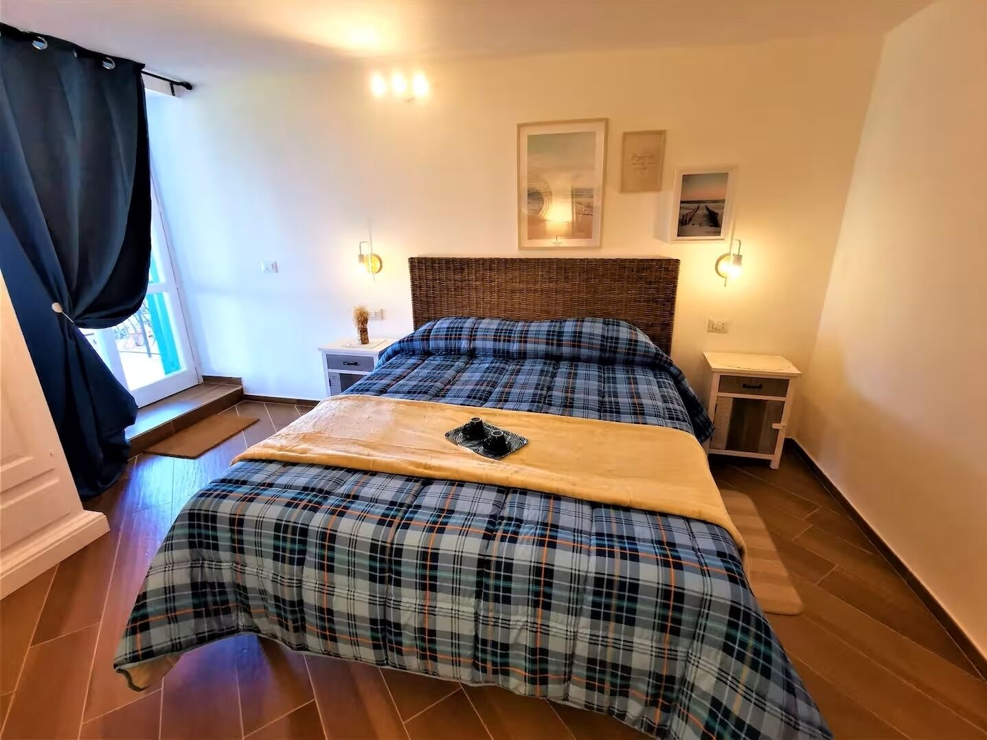 Une chambre à coucher comprenant un lit, une table de chevet, une commode, une fenêtre avec des rideaux et des lampes fixées au mur.