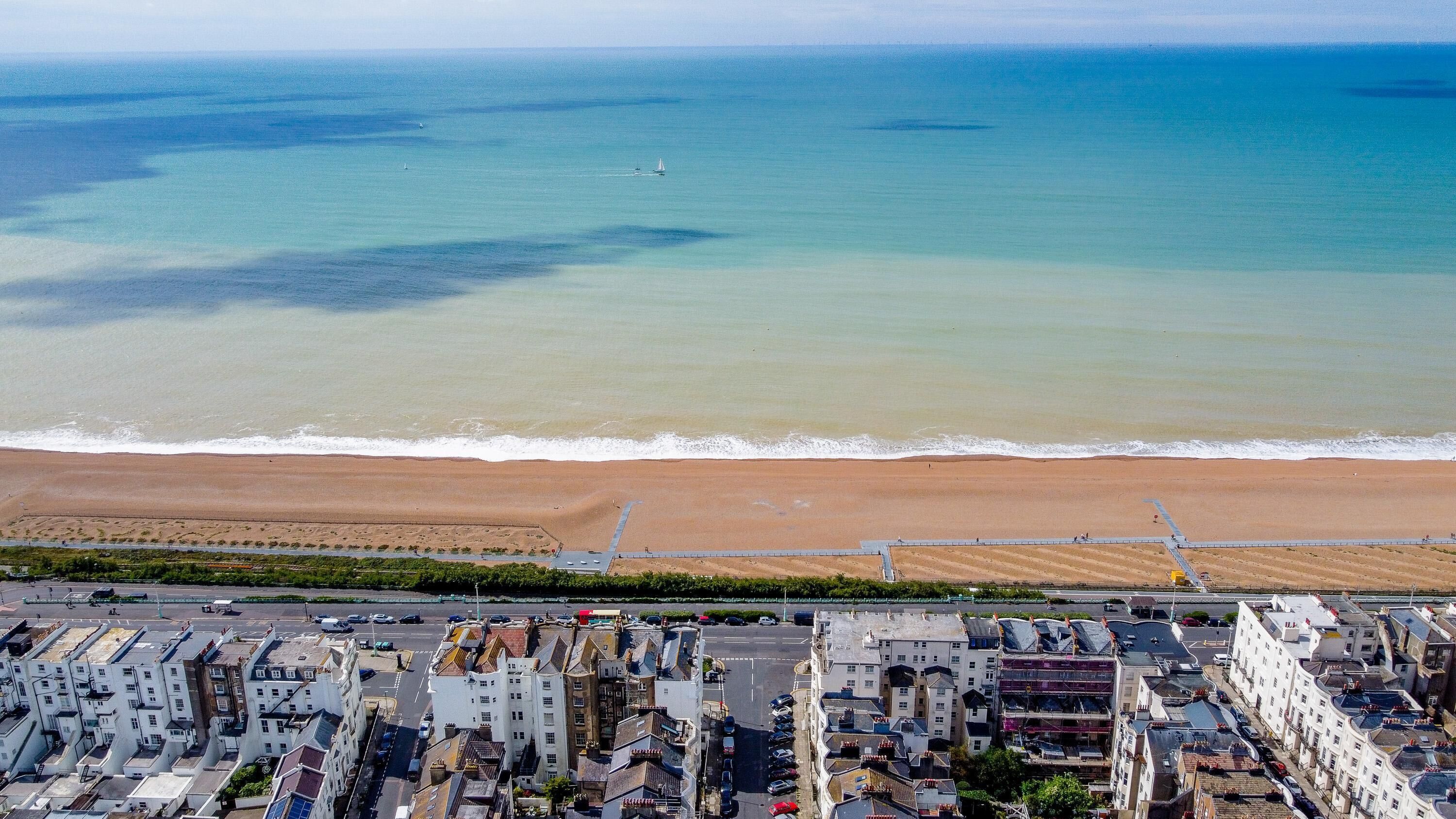 Uma vila costeira com uma praia de areia, um calçadão e edifícios residenciais.