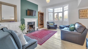 Una sala de estar con chimenea, televisor, sofá, sillón azul y alfombra roja.