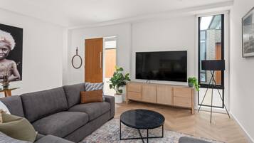 A modern living room with a grey sofa, a black coffee table, a flat-screen TV, and a potted plant.