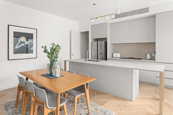 A modern kitchen with a central island, grey cabinets, a stainless steel refrigerator, and a built-in oven.