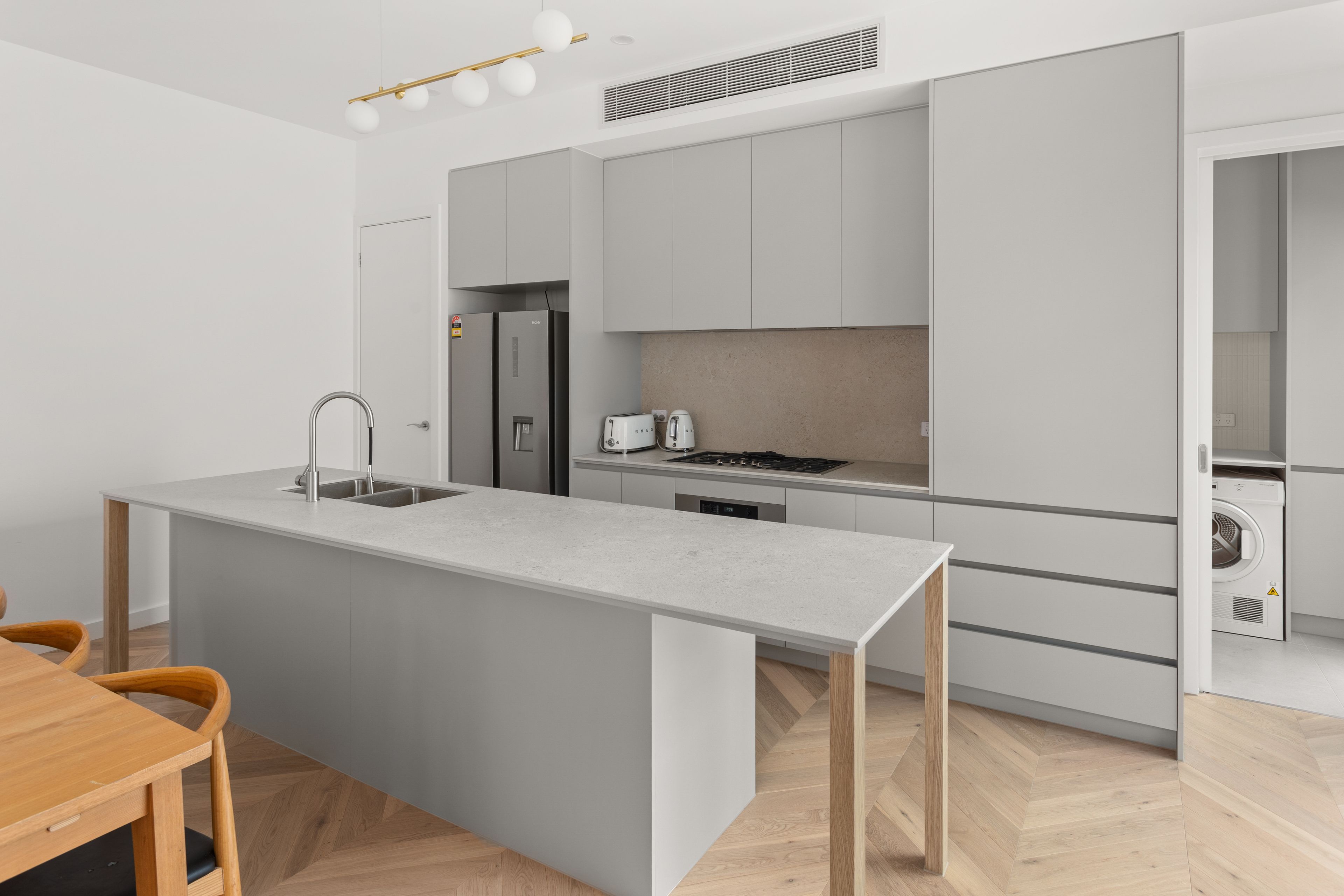 A modern kitchen with a central island, stainless steel appliances, and a herringbone wood floor.