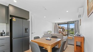 Una cocina moderna con un refrigerador empotrado, un comedor con mesa y sillas de madera, y vistas a un balcón con mobiliario exterior.