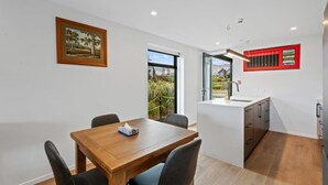 Una cocina moderna con una isla central, una zona de comedor con mesa de madera y vistas a través de un ventanal.