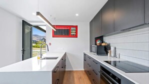 Una cocina moderna con una isla grande, muebles oscuros y un ventanal con marco rojo.