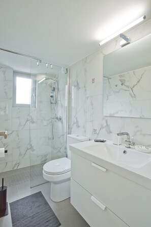Ein modernes Badezimmer mit einer gläsernen Duschkabine, einer weißen Toilette und einem großen Spiegel über einem weißen Waschbecken.