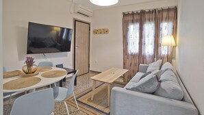 A modern living room with a flat-screen TV, a sofa, a dining table with placemats, and a lamp. - Athina in Chalandri With 2 Bedrooms and 1 Bathrooms (Chalandri)