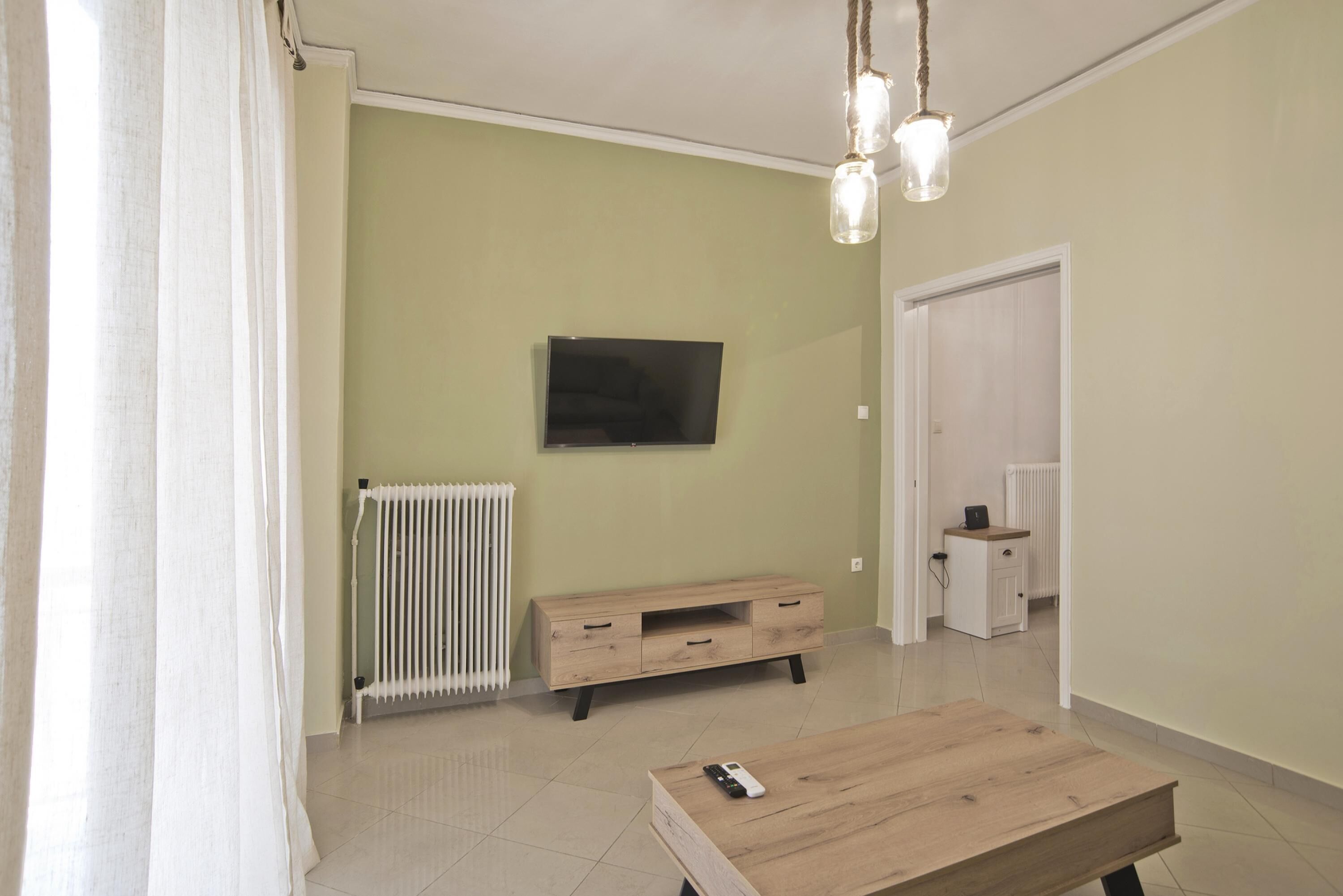 Una sala moderna con un televisor de pantalla plana montado en la pared, una mesa de centro de madera, un radiador y un armario blanco.