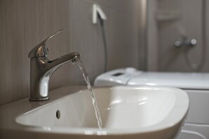 A bathroom sink with running water, a mirror, and a showerhead in the background. - Piraeus Wave in Piraeus (Piraeus)