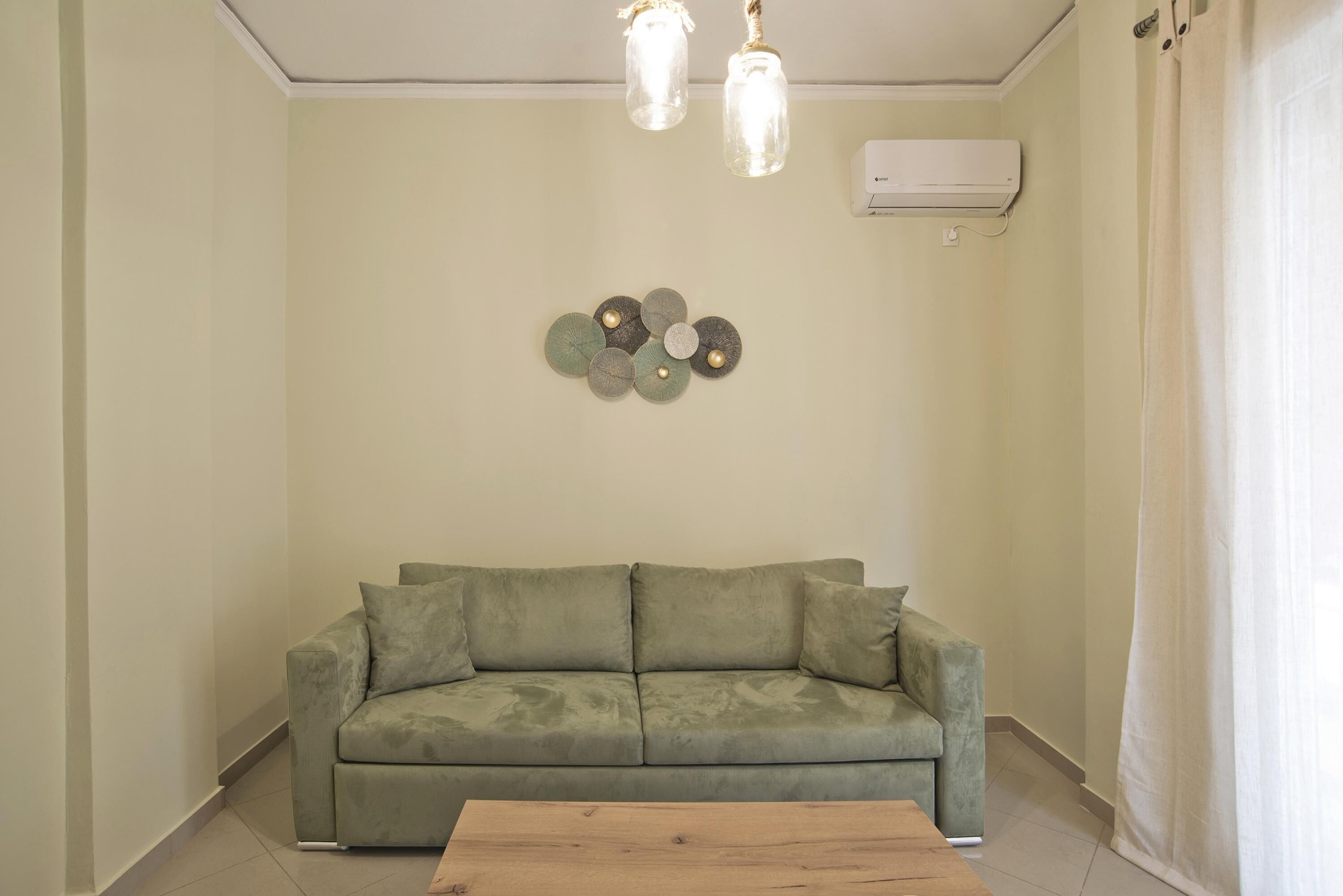 A living room with a green sofa, a wooden coffee table, and a wall-mounted air conditioner.