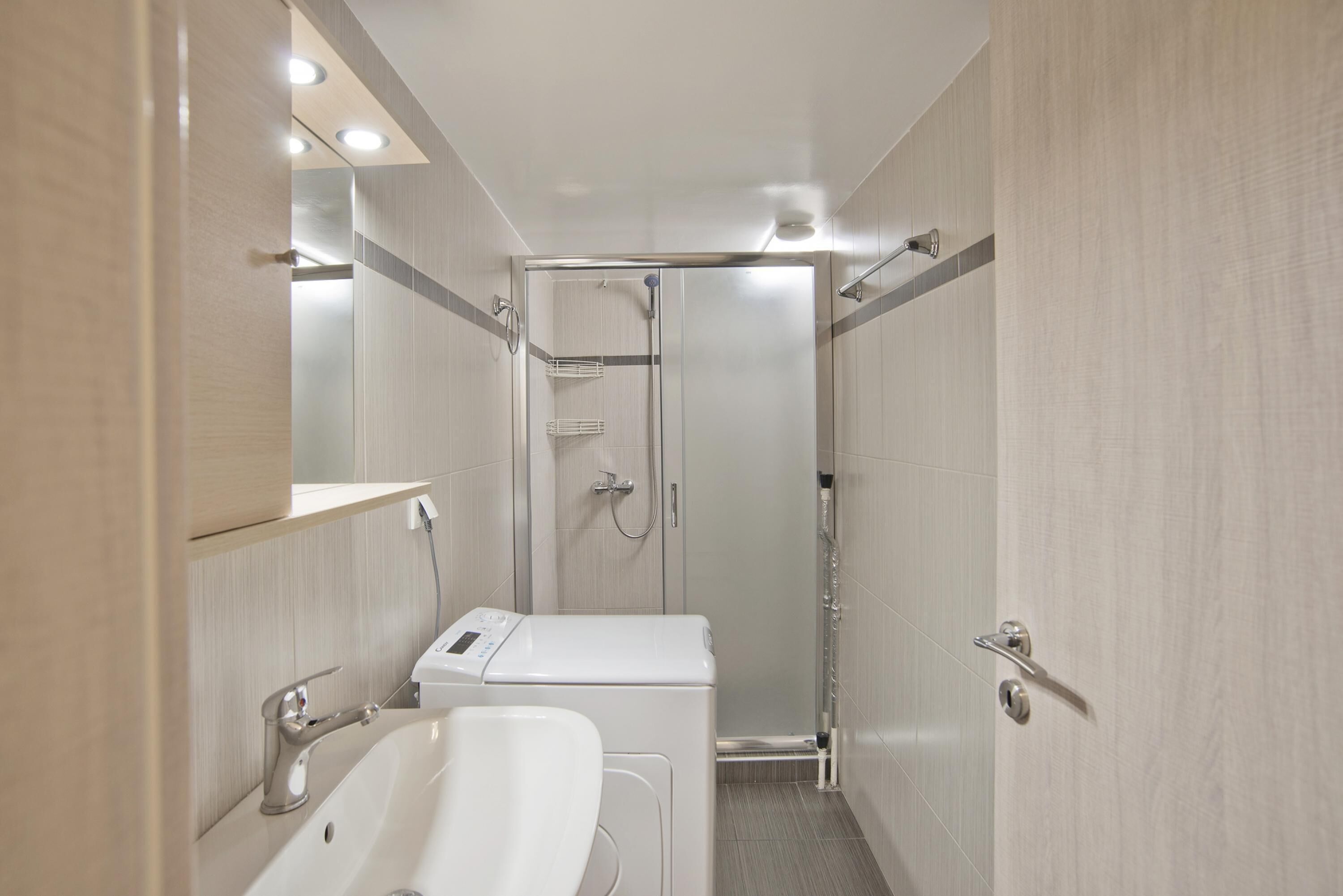 A compact bathroom with a shower, a sink, and a washing machine.