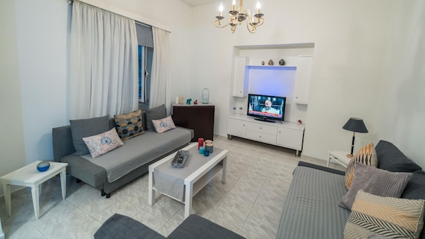 A modern living room with a grey sofa, a white coffee table, and a TV on a white cabinet. - Marina Apartment in Nikea (Nikaia-Agios Ioannis Rentis)