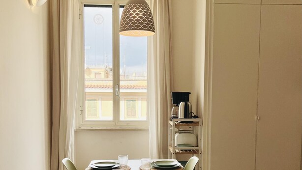 A dining area with a table set for four, green chairs, a hanging pendant light, and a view through a window. - Casa Duci in Rome With 2 Bedrooms and 1 Bathrooms (Rome)