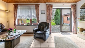 A room with a leather chair, a dining table with a vase of flowers, a radiator, and a view through a glass door.