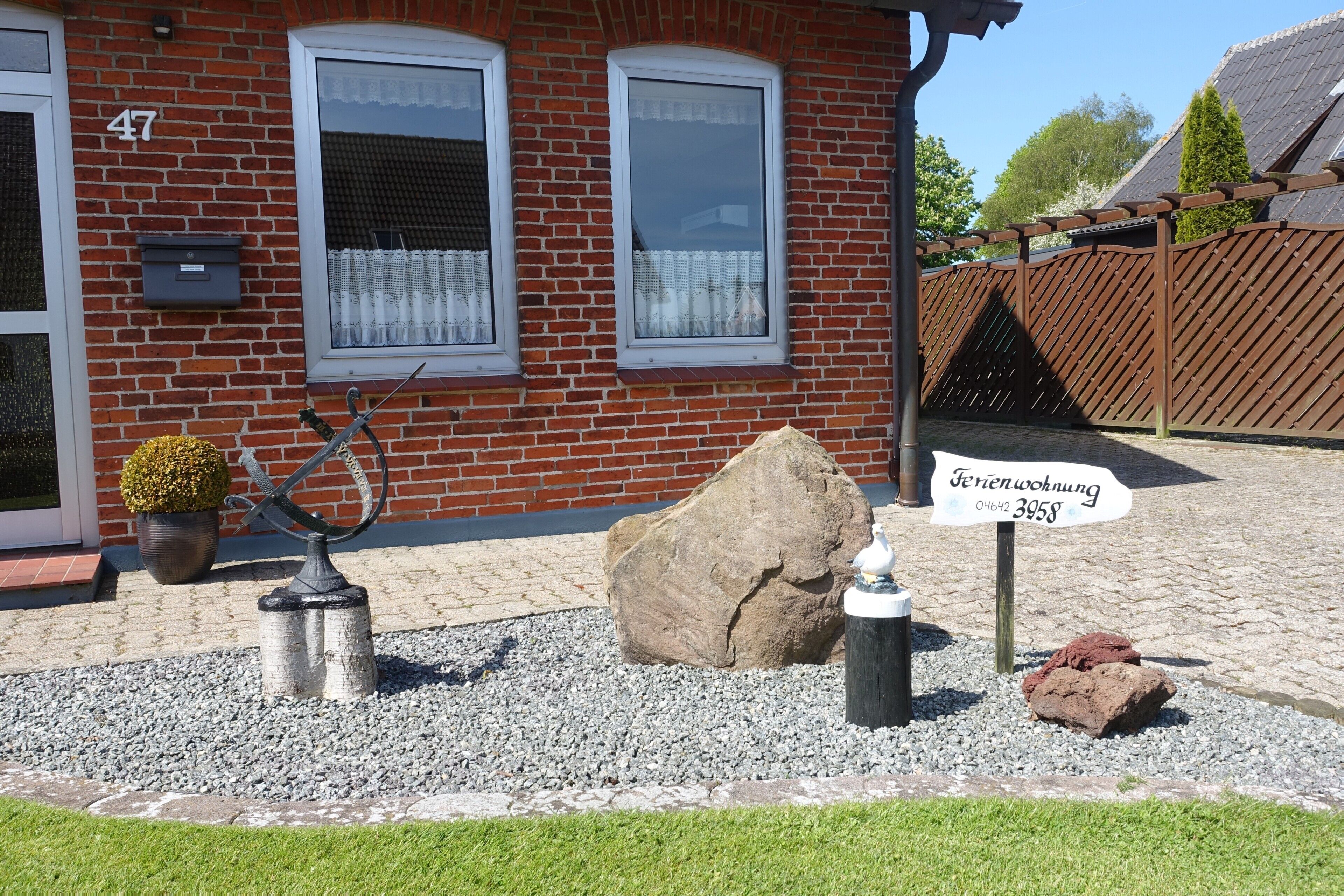 Een bakstenen huis met nummer 47, een grote rots, een metalen sculptuur en een bord met tekst.