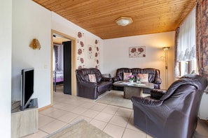 A living room with leather sofas, a coffee table, a TV, and a wooden ceiling.
